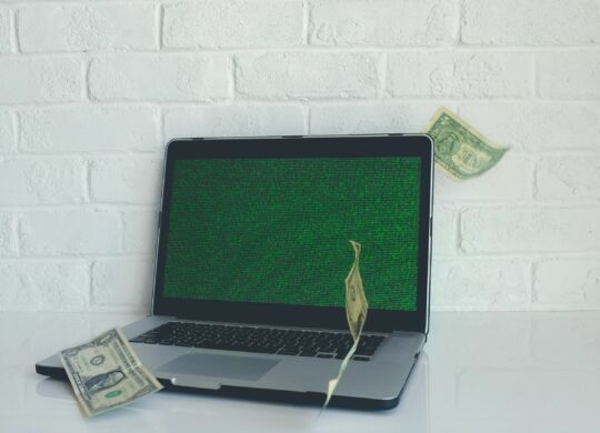 Kapitalfreisetzung: Macbook mit grünem Screensaver vor weißer Wand, es fliegen Geldscheine umher.